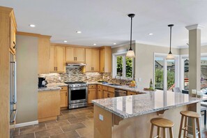 Une cuisine moderne avec des meubles en bois, des plans de travail en granit, des appareils électroménagers en acier inoxydable et des luminaires suspendus.