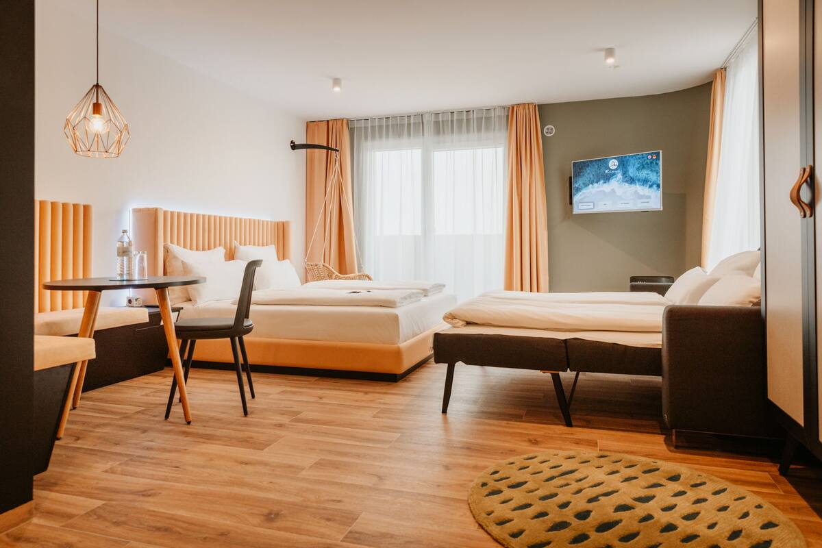 Quarto de hotel moderno com duas camas, um sofá, uma mesinha e uma televisão na parede.