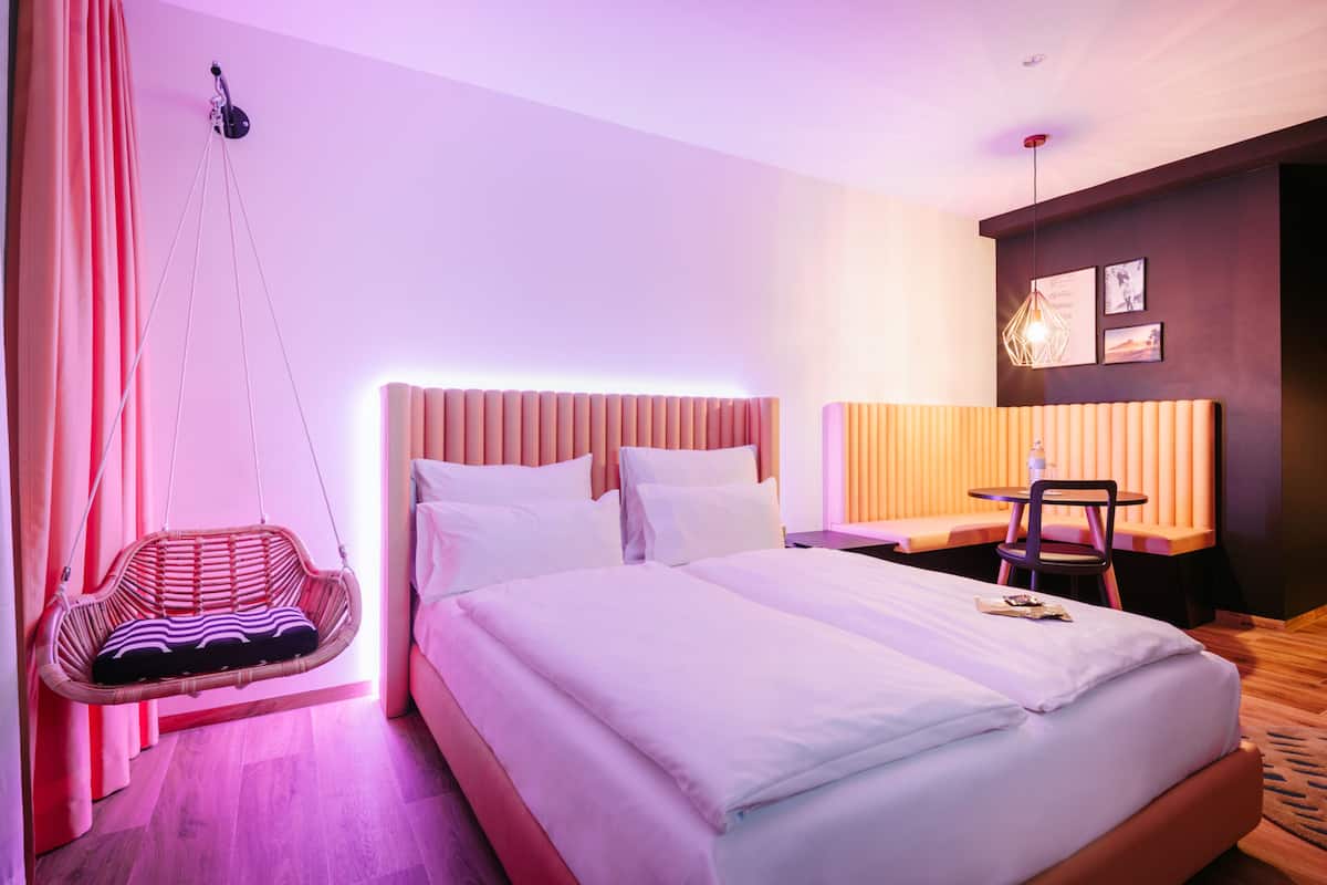 Quarto de hotel com cama grande, cadeira suspensa, escrivaninha e uma cadeira.