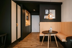 Interior moderno com piso de madeira, parede em preto e branco, armário de madeira com micro-ondas, mesa redonda com garrafa e um banco estofado.