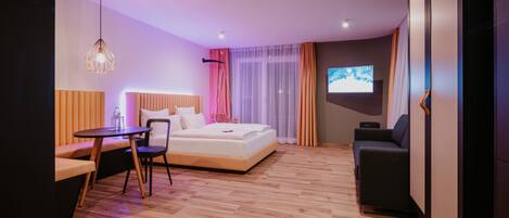 Una habitación de hotel moderna con una cama, un área de descanso con una mesa, un sofá y un televisor en la pared.