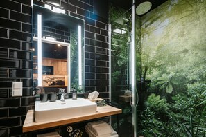 A bathroom with a black tiled wall, a white sink, and a shower with a glass door.