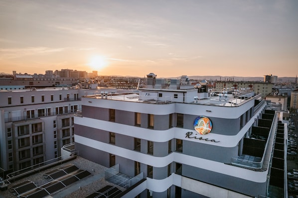 A multi-story building with a rooftop terrace, a visible logo, and a cityscape in the background. - Rioca Vienna Posto 2 (Vienna)