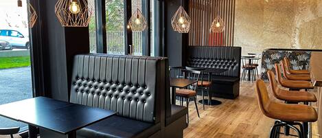 Un interior de restaurante moderno con cabinas tapizadas en negro, mesas de madera y taburetes de bar.