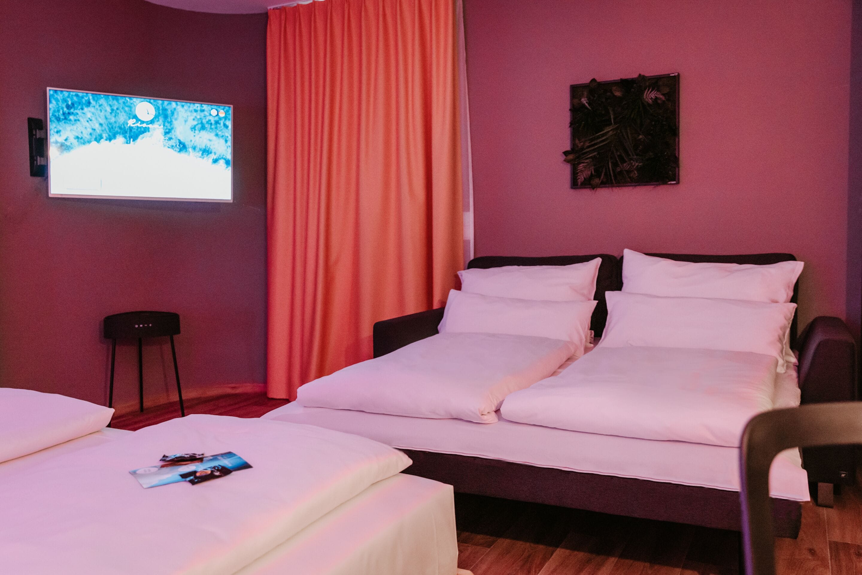 Ein Hotelzimmer mit einem Bett, einem kleinen Tisch, einem Sessel, einem Fernseher und einem Vorhang.