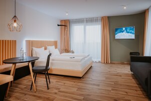 Quarto de hotel moderno com cama, mesa de jantar, cadeira, televisão e sofá.