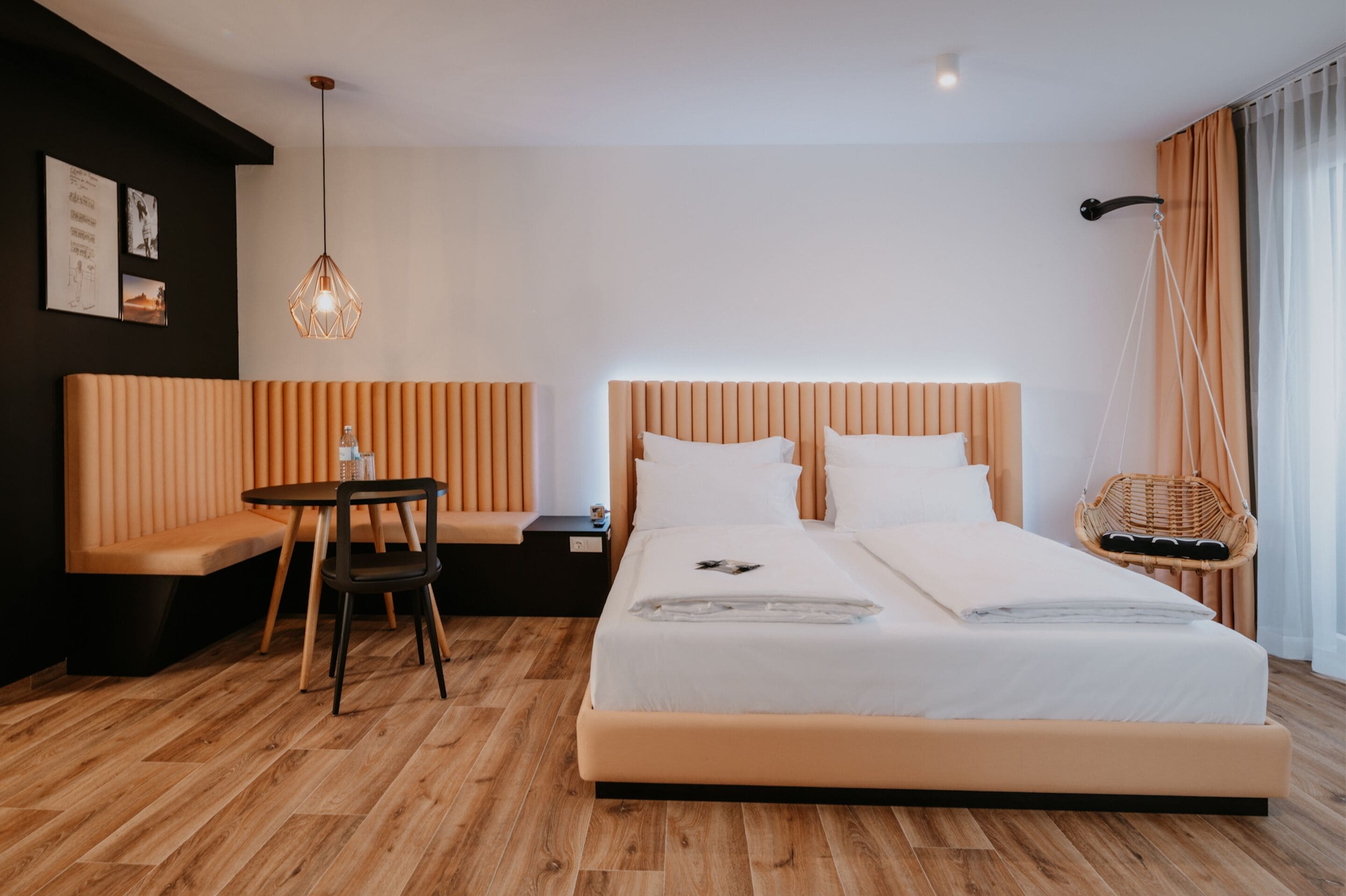 A modern hotel room with a large bed, a small table, a bench, and a hanging chair.