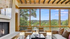 A spacious living room with a fireplace, large windows, and a view of the landscape. - Above Waterfalls I Premier | Party Dock I Pool I Theater I Luxury I Services (Austin)