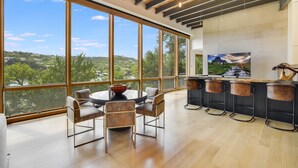 A modern kitchen with large windows, a dining area, and a bar with stools. - Above Waterfalls I Premier | Party Dock I Pool I Theater I Luxury I Services (Austin)