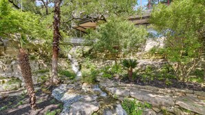 A serene garden with a small waterfall, stone pathways, and lush greenery. - Above Waterfalls I Premier | Party Dock I Pool I Theater I Luxury I Services (Austin)