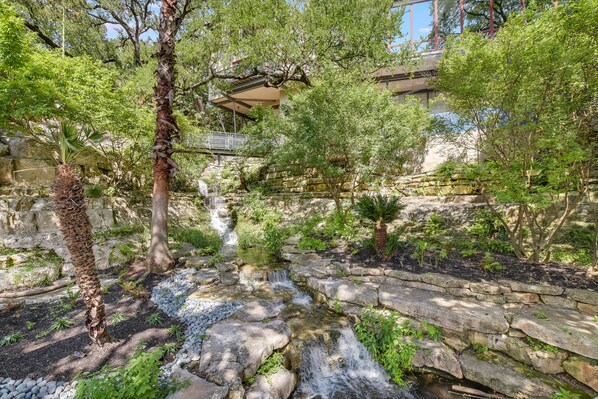 Ein friedlicher Garten mit einem kleinen Wasserfall, Steinwegen und üppigem Grün.