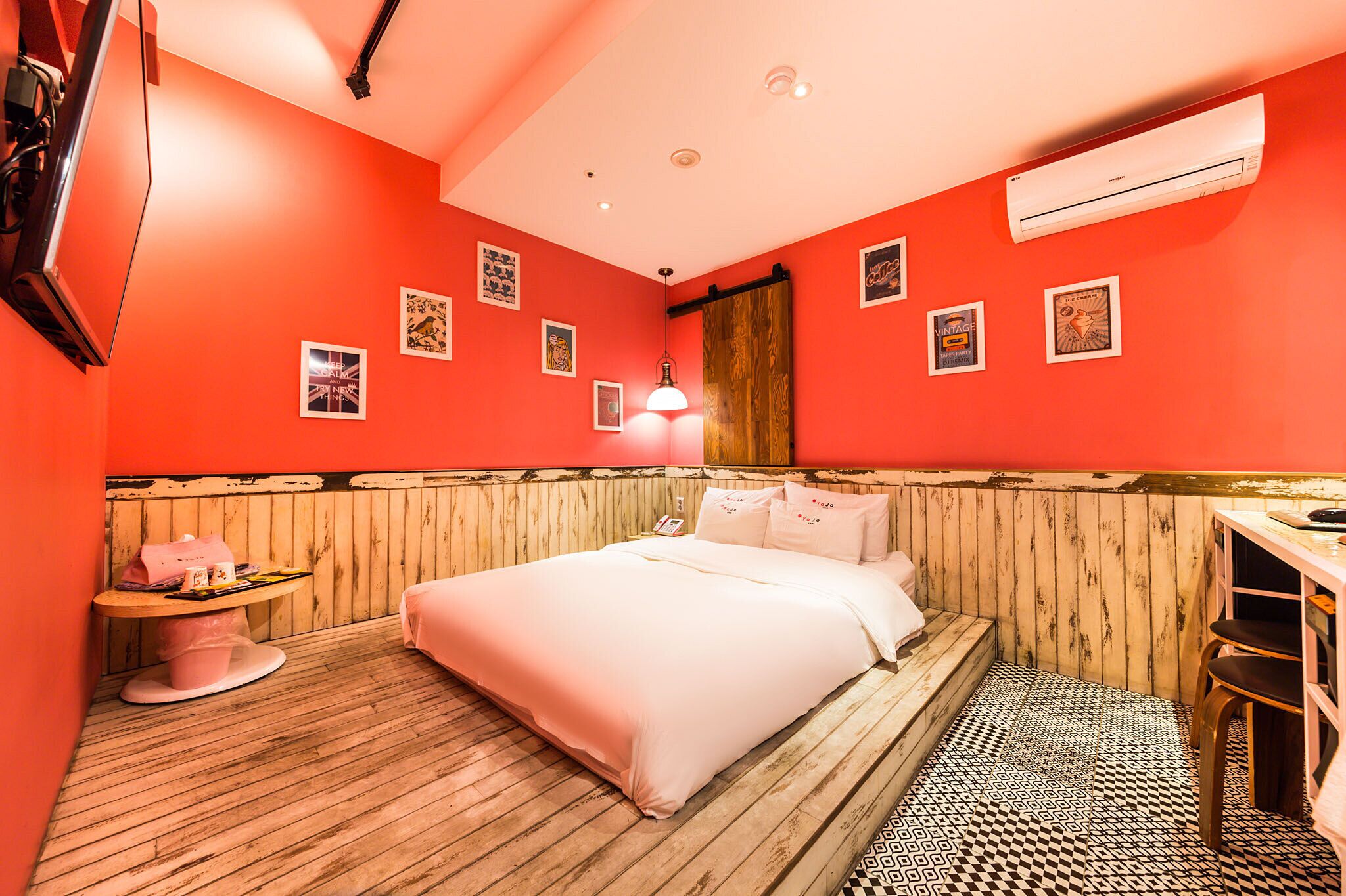 A room with a bed, a desk, and a chair. There are pictures on the wall and an air conditioner above the bed.
