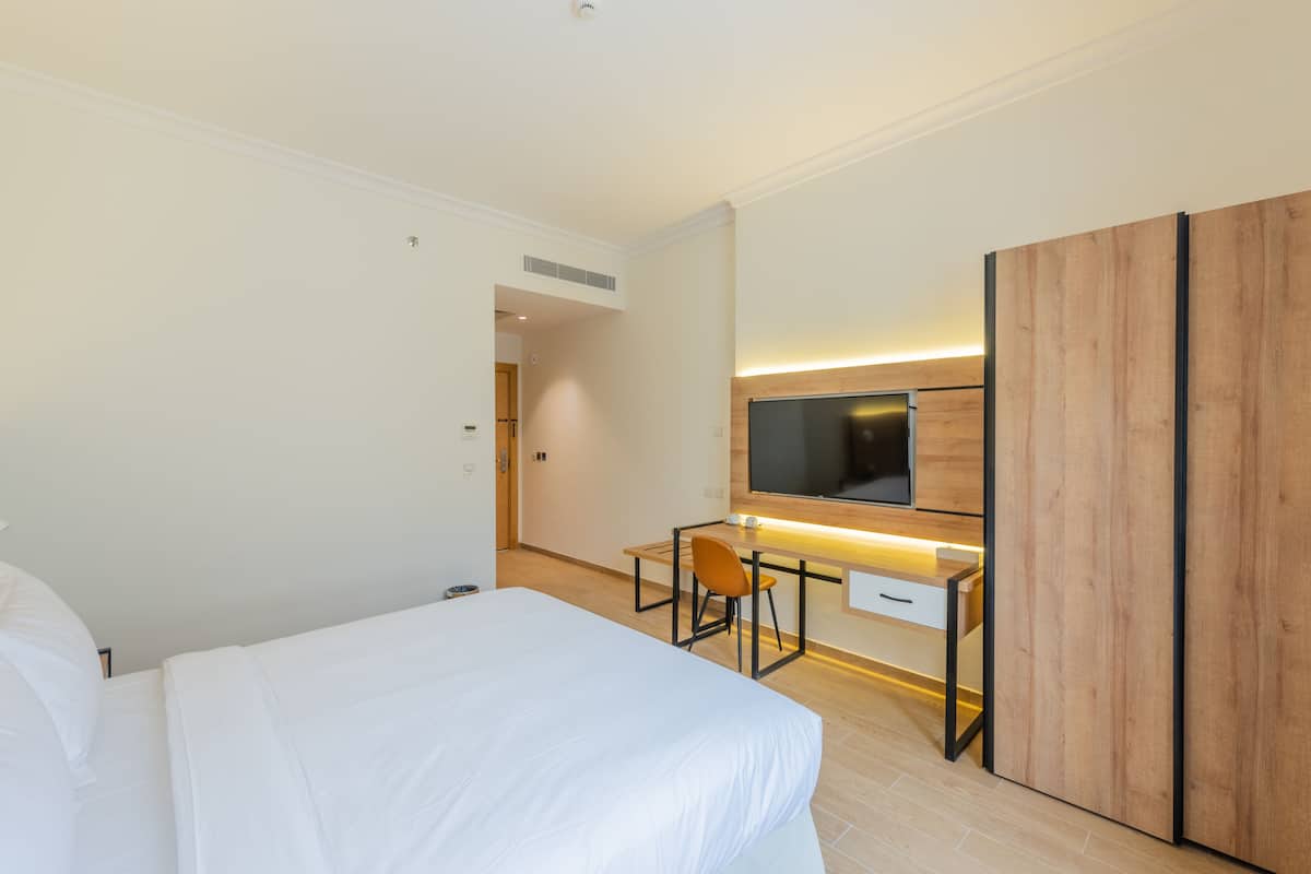 A hotel room with a bed, a desk with a chair, a TV mounted on the wall, and a wardrobe.