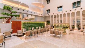 A spacious lobby with a seating area, a large tree, and a green wall with a patterned design. - Hasanah Suites for Serviced Apartments. (Madinah)