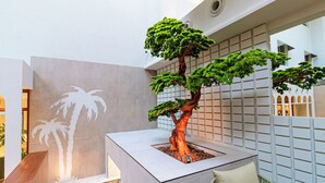 Un interior moderno con un bonsái como pieza central, un diseño geométrico en la pared y una silla de mimbre.