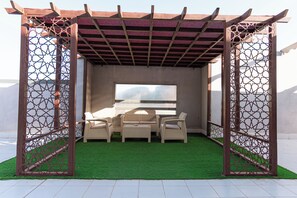 A covered outdoor seating area with artificial grass, a sofa set, and a large window.