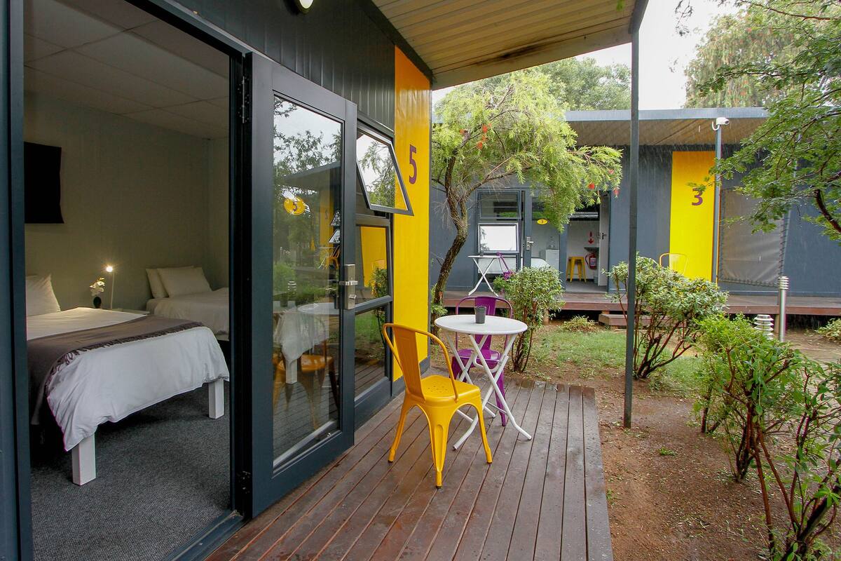 A modern outdoor area with a bed, a yellow chair, and a small table.