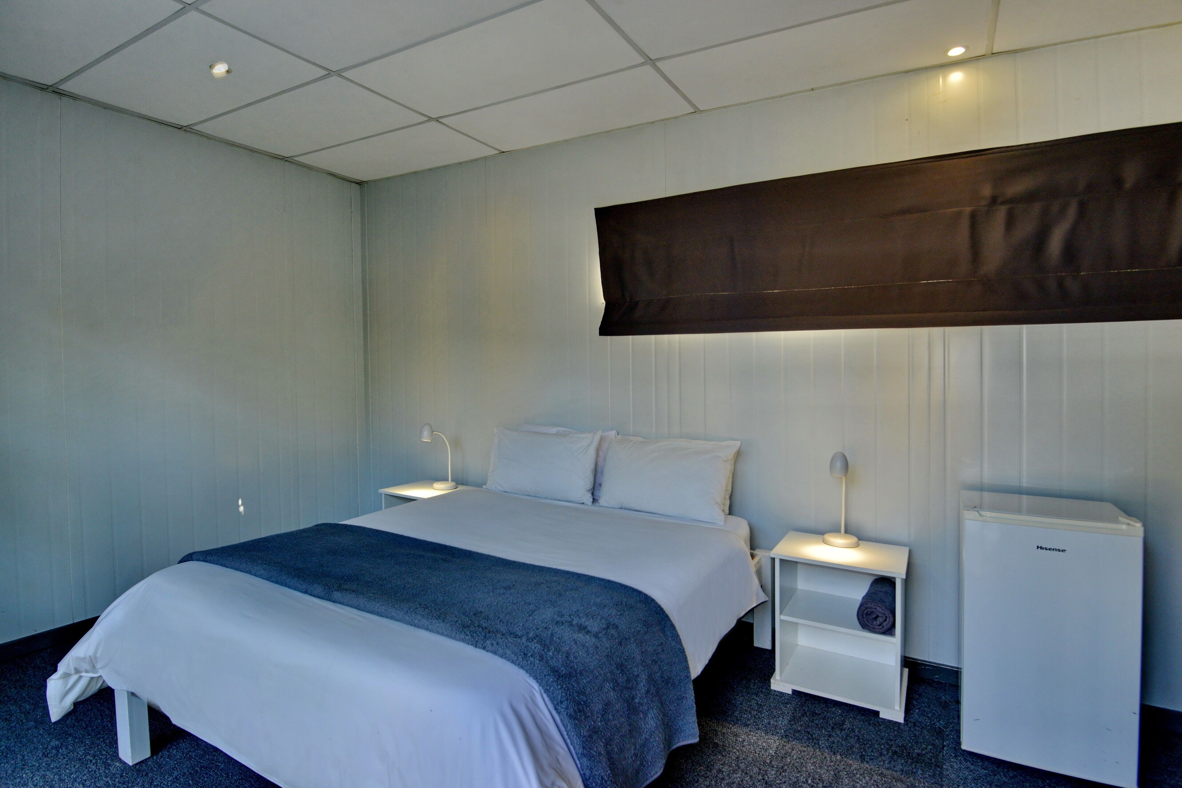 Una habitación de hotel con una cama grande, una mesita de noche, una lámpara y un electrodoméstico pequeño y blanco.