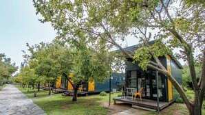 Filas de cabañas modernas con arbolado y zonas de estar exteriores, junto a un sendero de piedra.