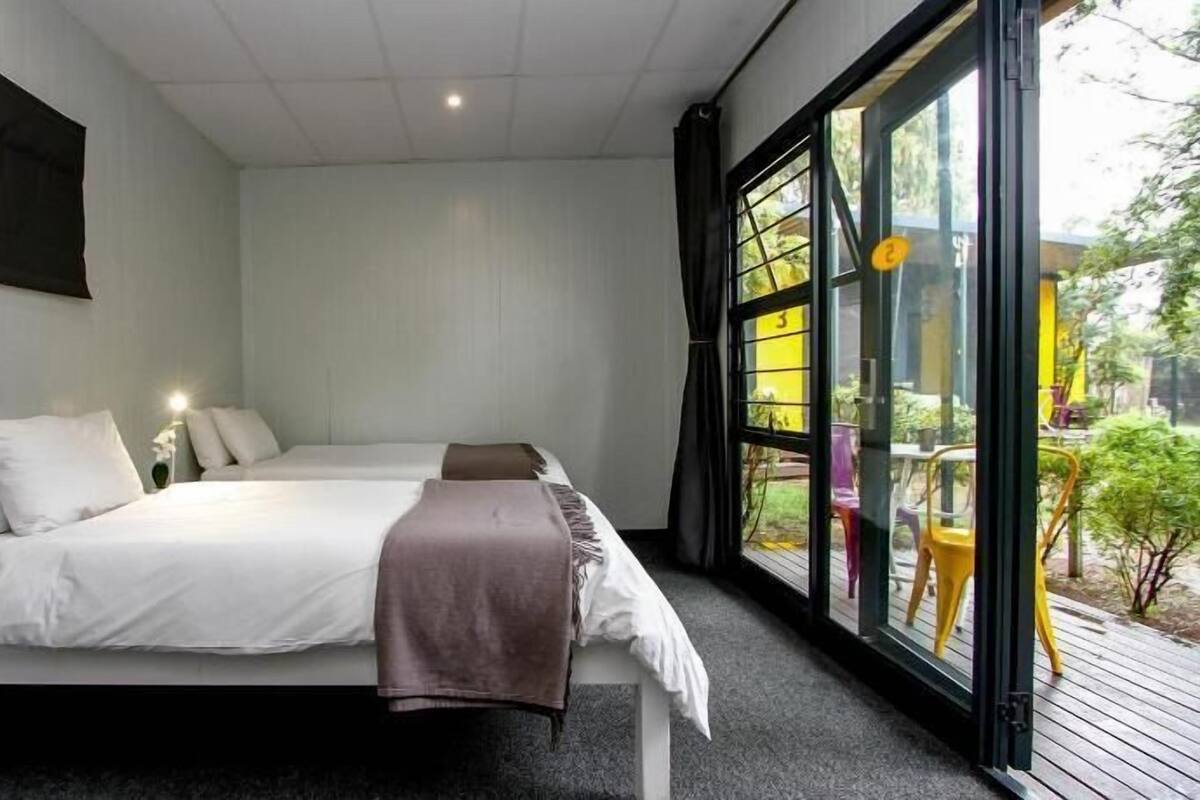 A bedroom with two beds, a window with a view of the outdoors, and a small table with chairs outside.