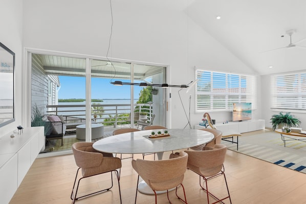 A modern interior with a round dining table surrounded by chairs, a large window with blinds, and a view of the outdoors.