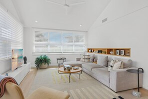 A modern living room with a sofa, coffee table, and a TV. There is a plant, a small side table, and a shelf with decorative items. - GORGEOUS UPSCALE LONGBOAT KEY CONDO OFFERS BAYFRONT VIEWS!! (Longboat Key)