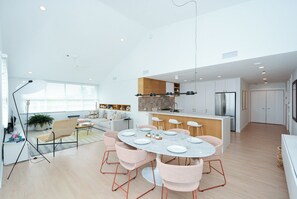 Une cuisine spacieuse dotée d’un îlot central, un coin repas avec une table ronde et des chaises, et un salon avec un canapé et une table basse.