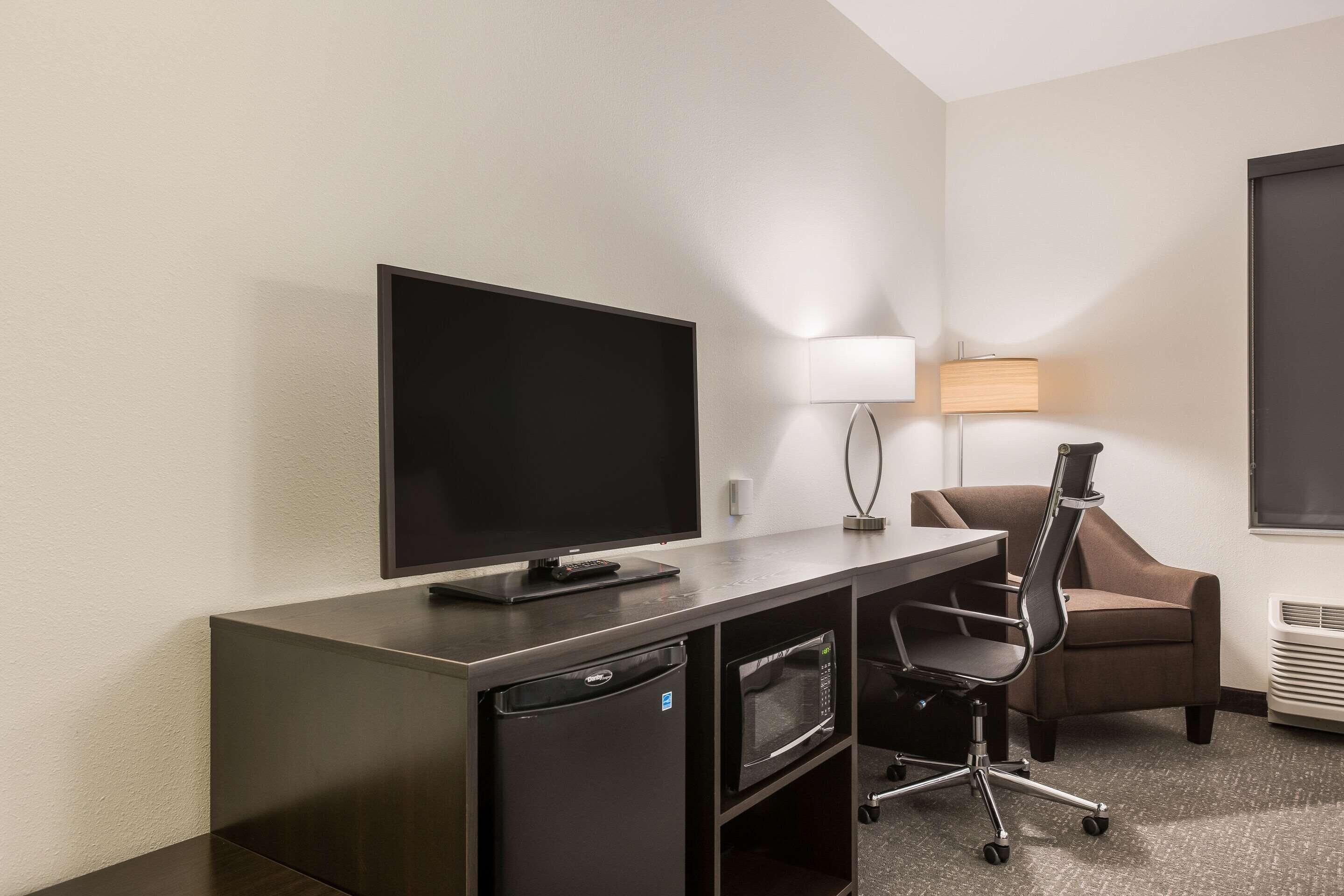 A hotel room with a flat-screen TV, a desk with a lamp, a microwave, and a chair.