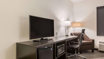 A hotel room with a flat-screen TV, a desk with a lamp, a microwave, and a chair.
