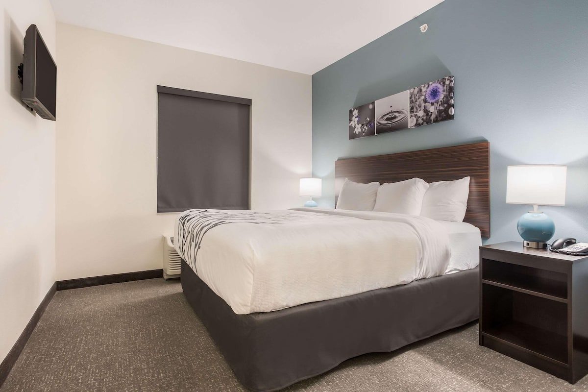 A hotel room with a bed, bedside lamps, a flat-screen TV, a window, and artwork on the wall.