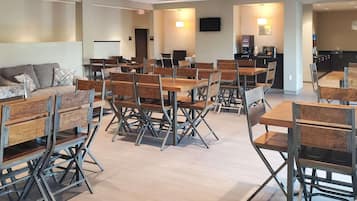 A modern hotel lobby with multiple seating areas, including a sofa and tables with chairs.