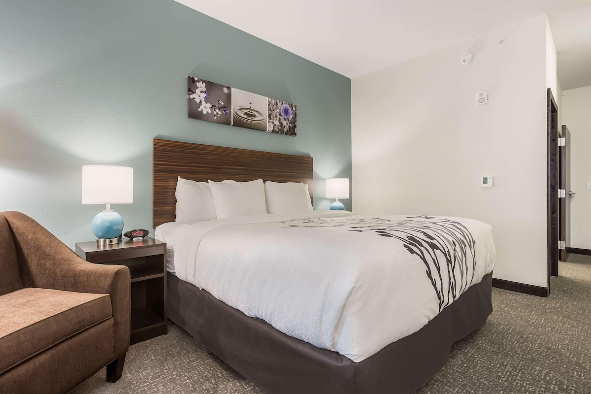 A hotel room with a bed, a nightstand, a lamp, and a chair.