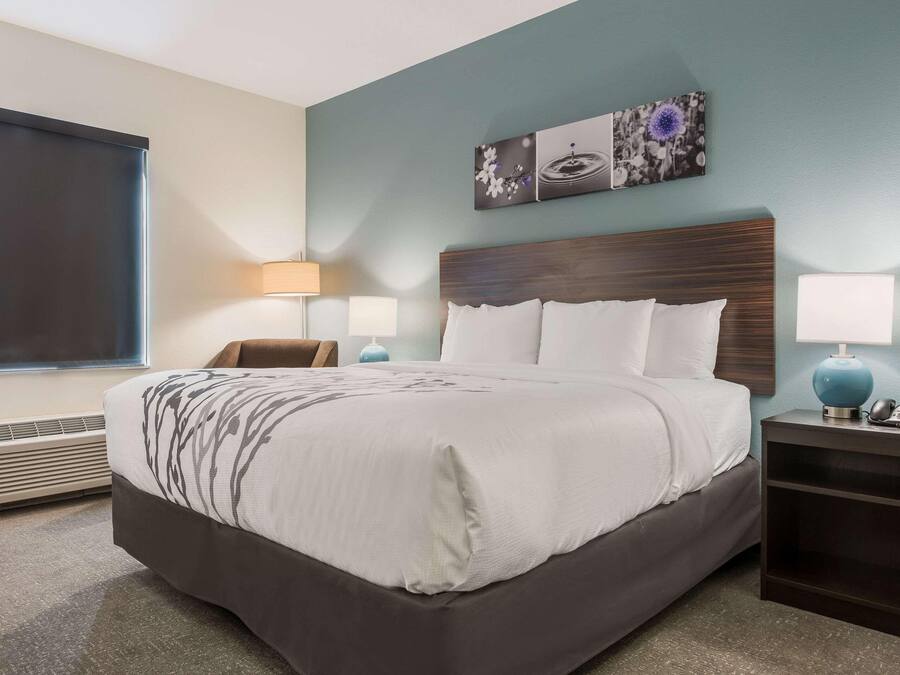 A neatly arranged hotel room with a bed, bedside tables, a wall-mounted artwork, and a window with blinds.