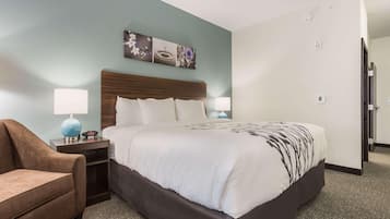 A hotel room with a bed, a nightstand, a lamp, and a chair.