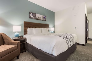 A hotel room with a bed, a nightstand, a lamp, and a chair. - Sleep Inn & Suites Webb City (Webb City)
