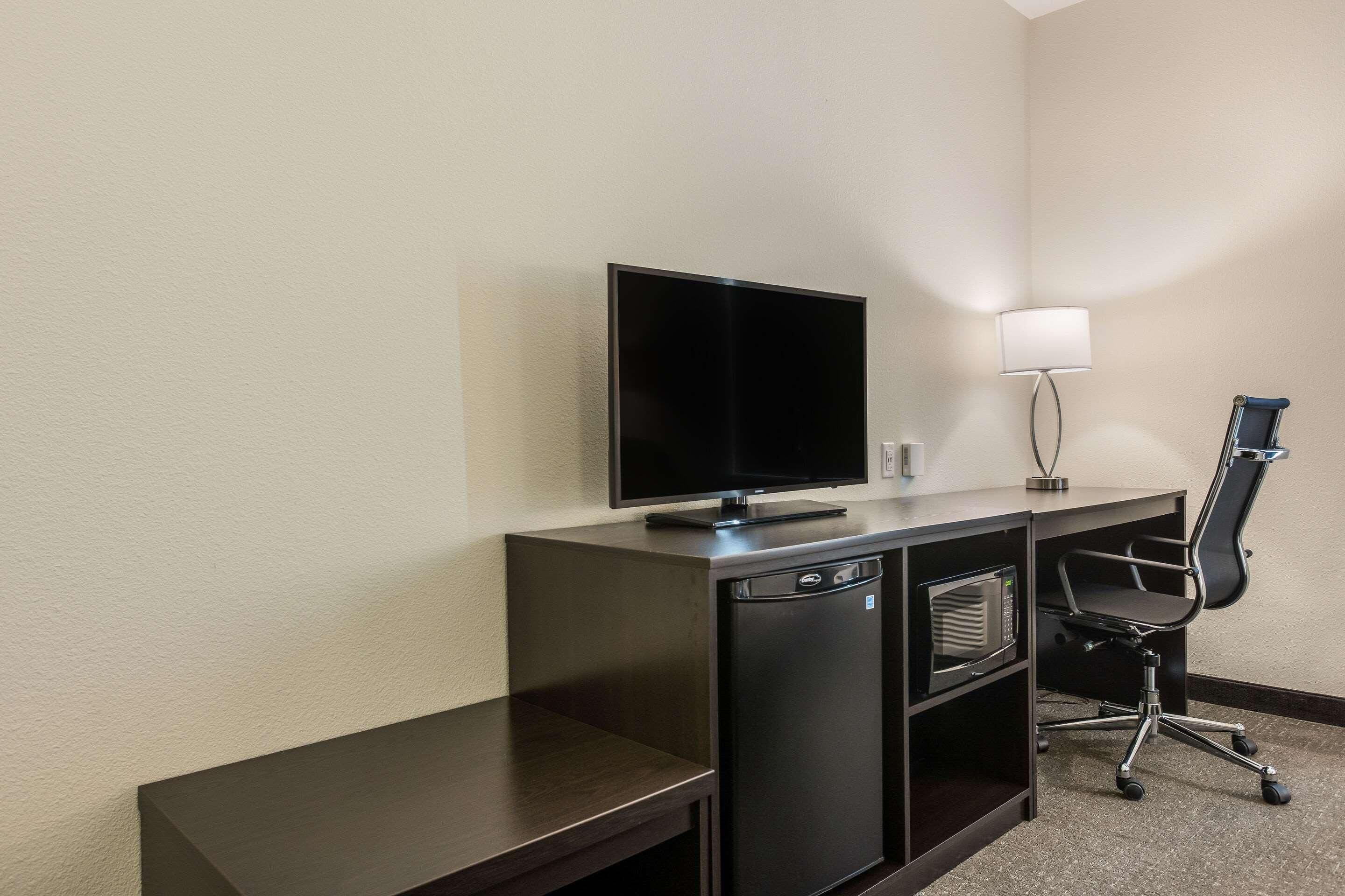 A compact hotel room with a dark wooden desk, a flat-screen TV, a microwave, and a black office chair.