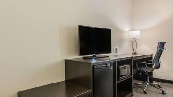 A compact hotel room with a dark wooden desk, a flat-screen TV, a microwave, and a black office chair.