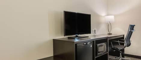 A compact hotel room with a dark wooden desk, a flat-screen TV, a microwave, and a black office chair.