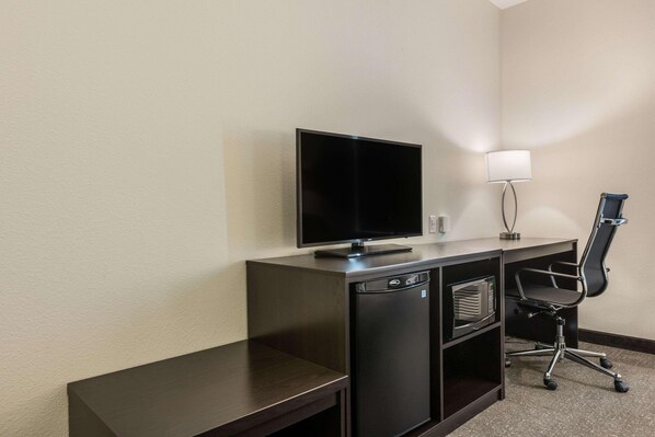 A compact hotel room with a dark wooden desk, a flat-screen TV, a microwave, and a black office chair.