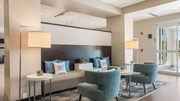 A modern hotel lobby with a sofa, two armchairs, a round table, and a floor lamp.