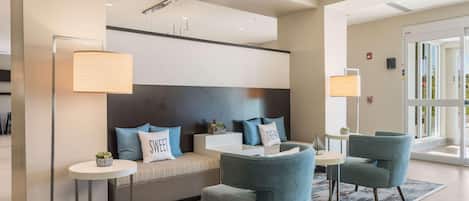 A modern hotel lobby with a sofa, two armchairs, a round table, and a floor lamp.