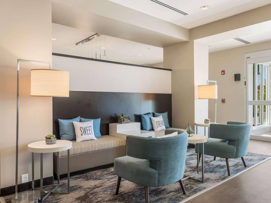 A modern hotel lobby with a sofa, two armchairs, a round table, and a floor lamp.