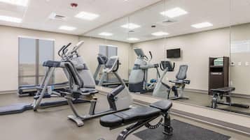 Une salle de sport équipée de divers appareils d’exercice, notamment des tapis de course et des vélos d’appartement, et dotée d’un grand miroir mural.