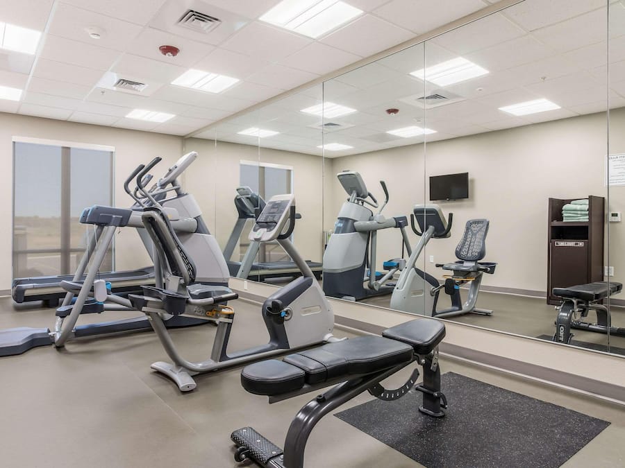 Un gimnasio con diversos equipos de ejercicio, incluyendo cintas de correr y bicicletas estáticas, y un espejo grande en la pared.