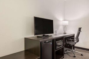 A compact hotel room with a flat-screen TV, a small refrigerator, a desk, a chair, and a lamp. - Sleep Inn & Suites Webb City (Webb City)
