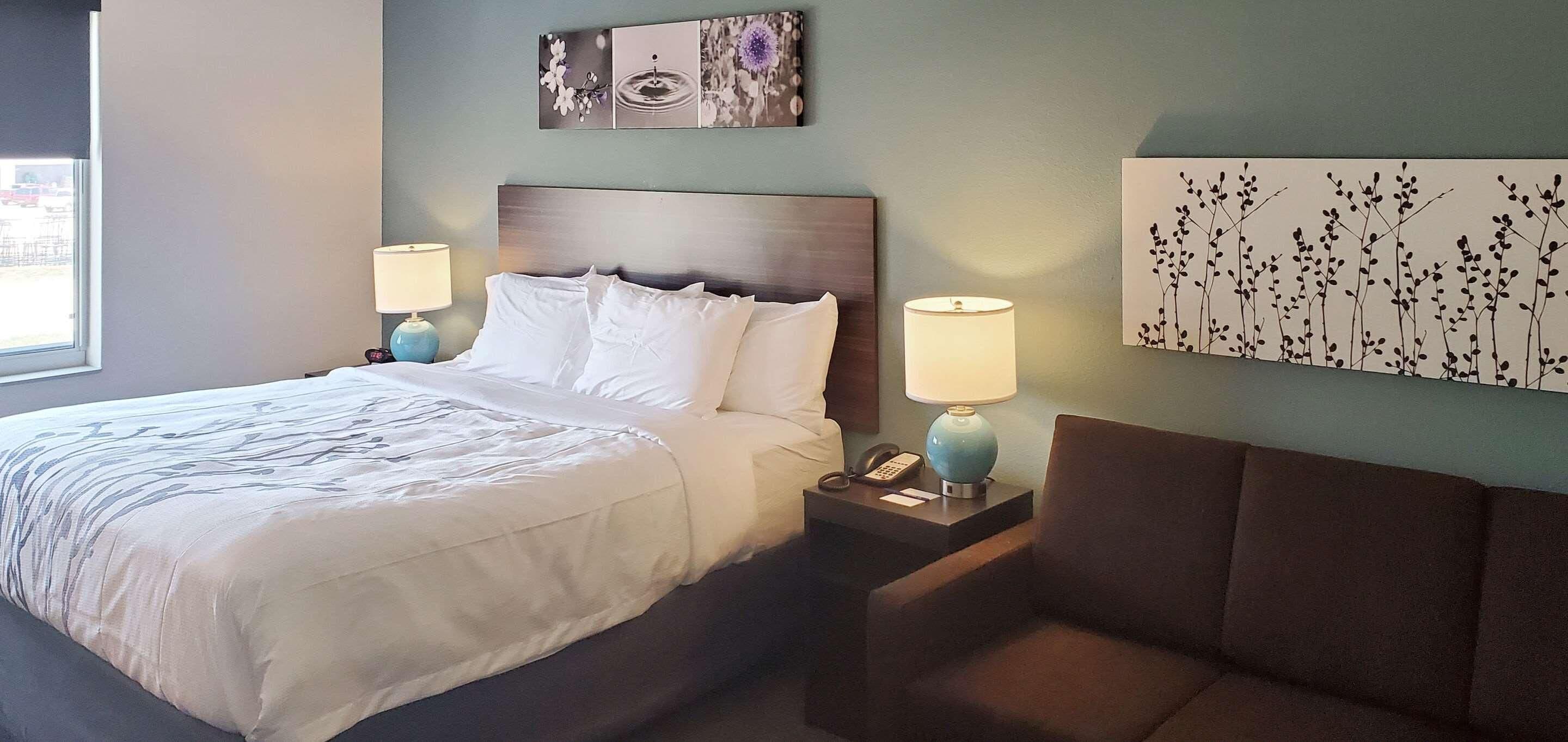 Een hotelkamer met een bed, twee bedlampen, een nachtkastje, een telefoon en een kunstwerk boven het bed.