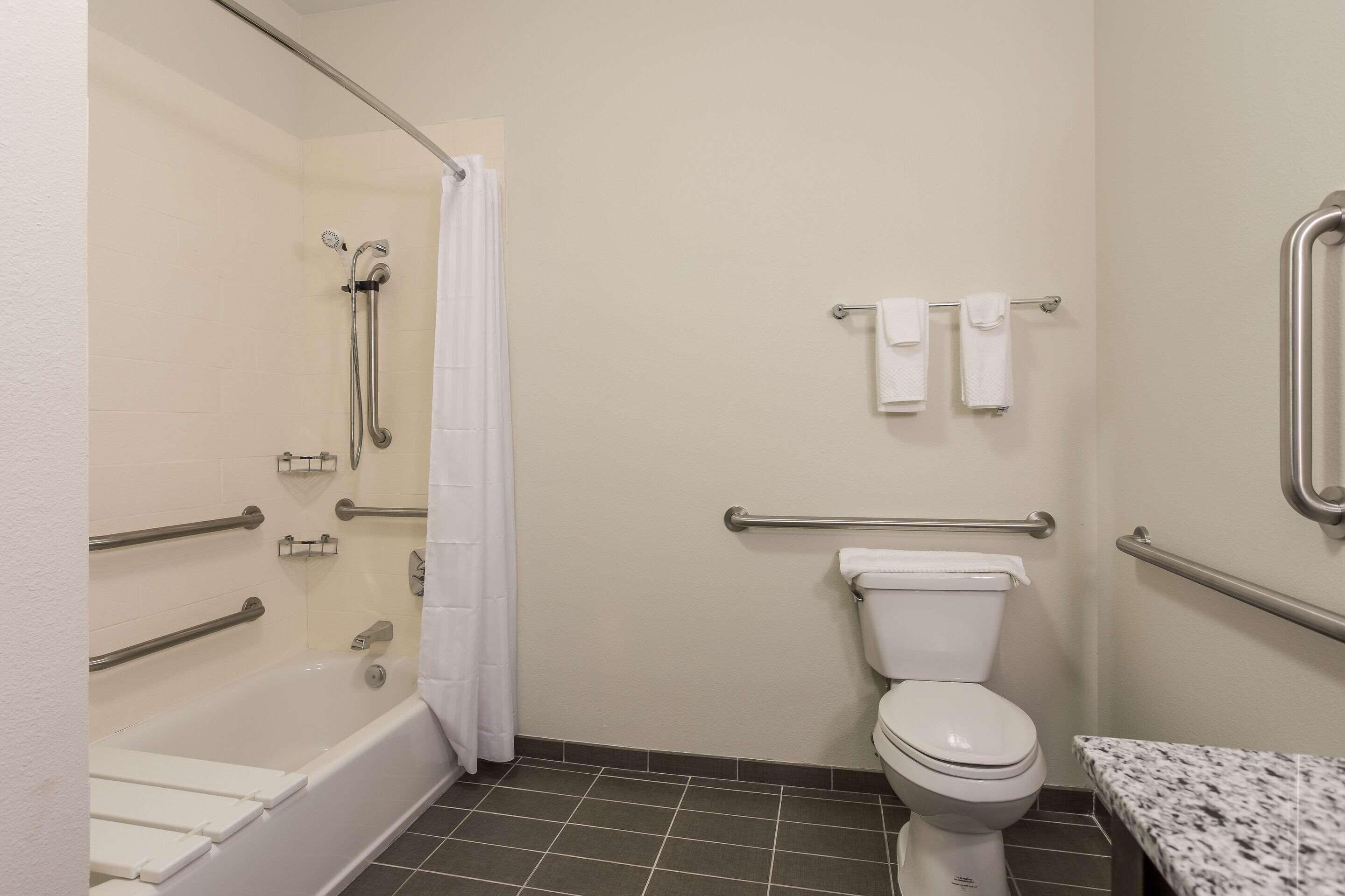 A bathroom with a bathtub, toilet, and grab bars.