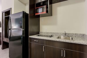 A kitchen with a black refrigerator, a granite countertop, a stainless steel sink, and dark wooden cabinets. - Sleep Inn & Suites Webb City (Webb City)