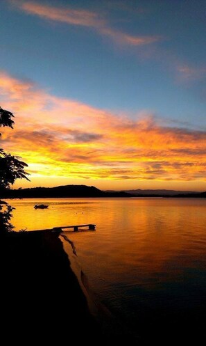 A sunset over a calm lake with a dock and trees on the left.
