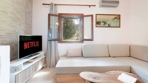 Un saló modern amb un sofà blanc, una taula de centre de fusta, un televisor que mostra 'NETFLIX', una finestra amb cortines i un quadre a la paret.